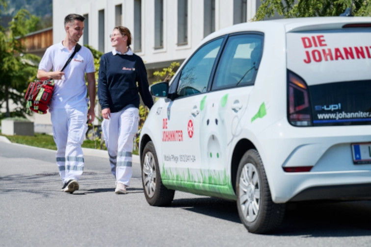 Zwei Pfleger:innen stehen neben einem Auto: Mobile Pflege